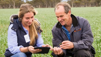 Two people in green crop reviewing data on digital device