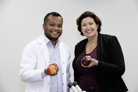 A man and woman standing smiling and holding Cripps Pink variety apples.