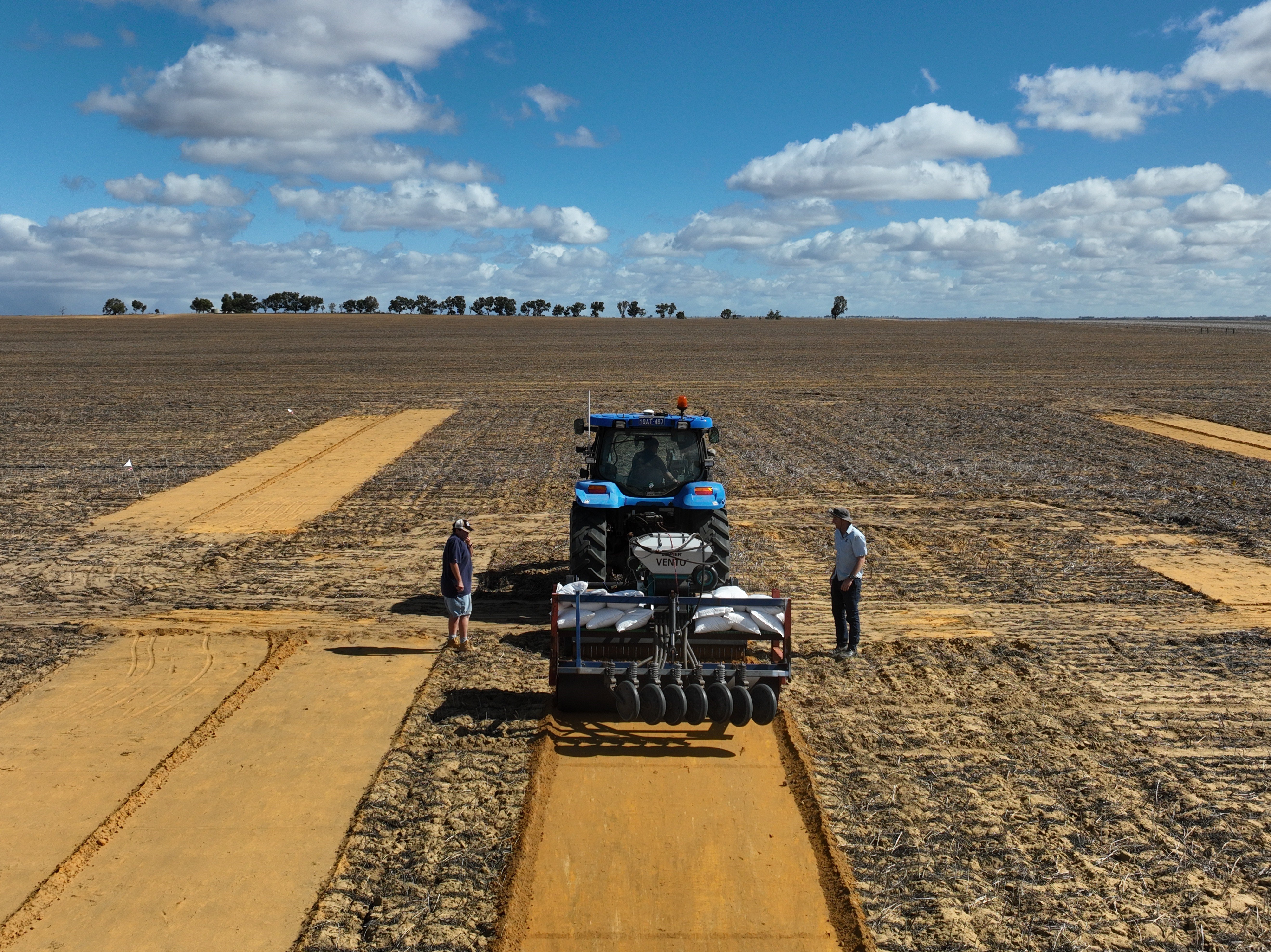 Bare paddock of stubble with tractor and 2 men