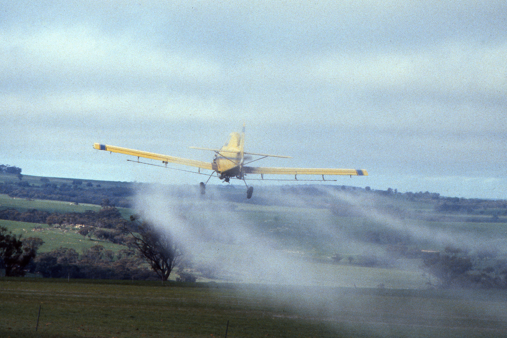 A small, 1-person plane is flown low over crops to perform aerial spraying.