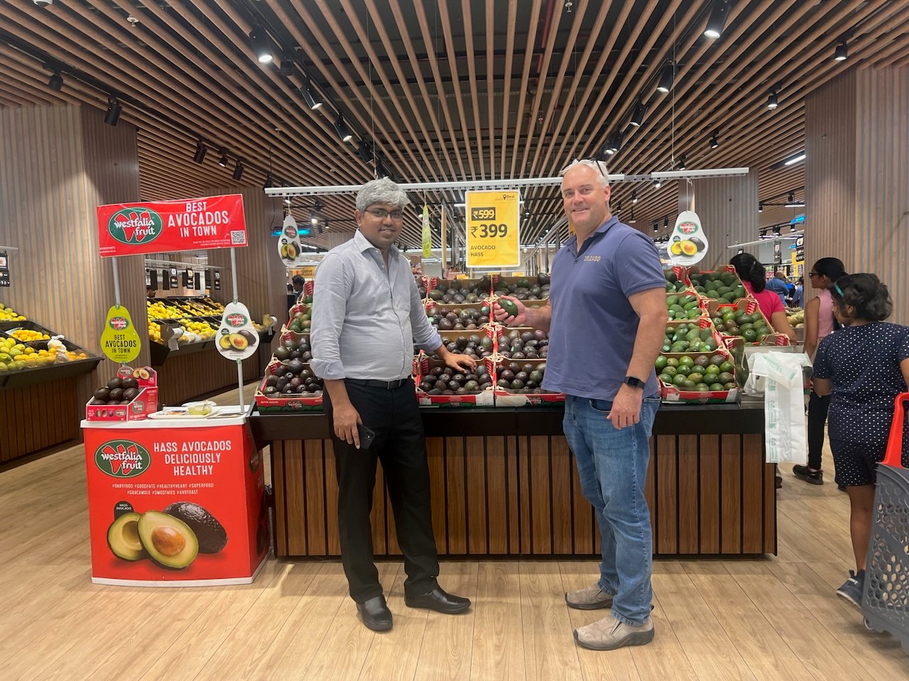 2 men standing against a display of avocados in an Indian supermarket