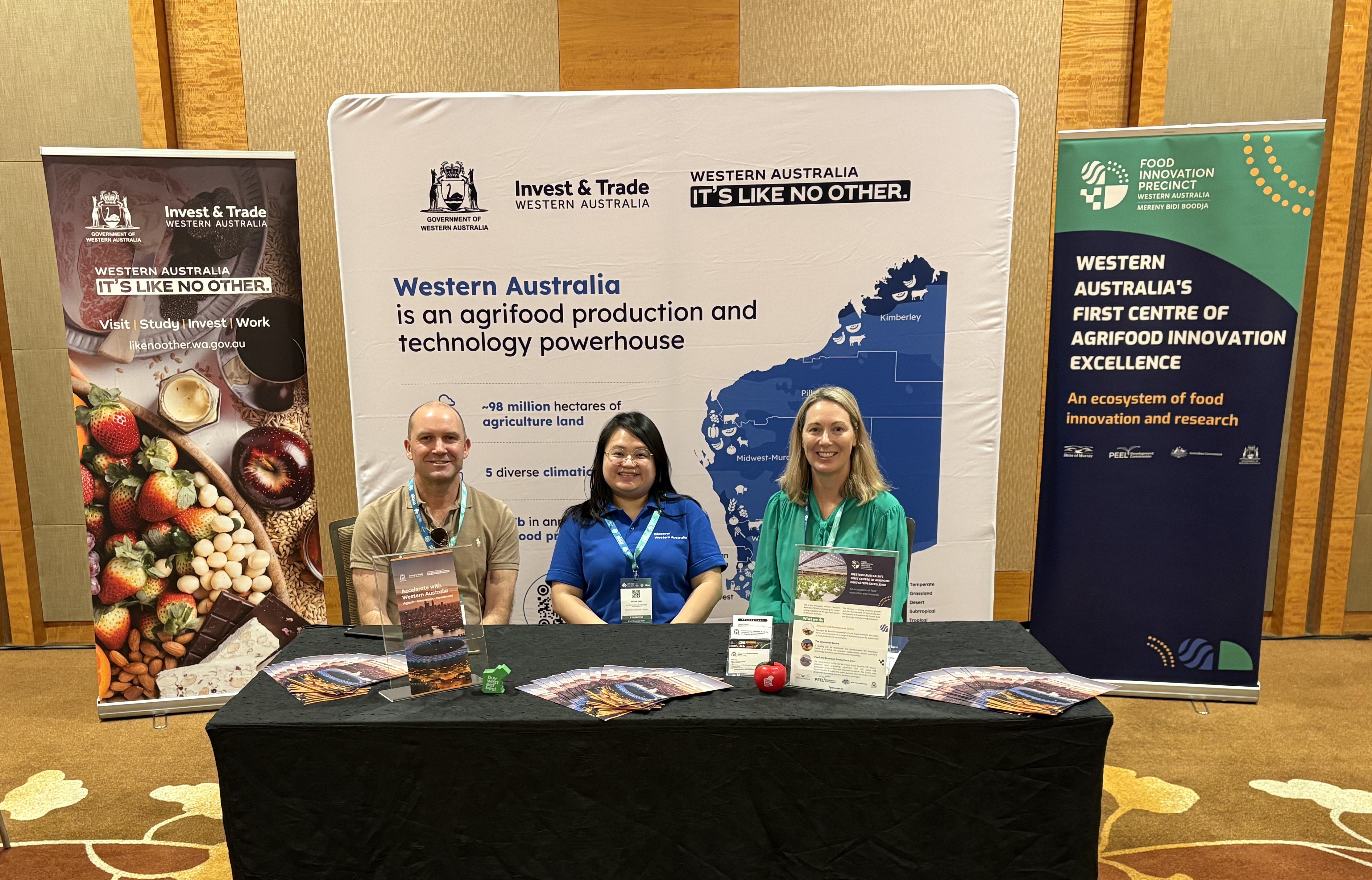 A male and two female sitting at a desk infront of a Western Australian banner 