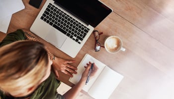 Overhead view of person writing in notebook next to laptop computer