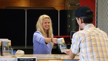 Two people one handing a brochure to another from behind counter