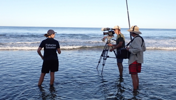 Camera and sound person filming Fisheries Education Officer at beach for media item