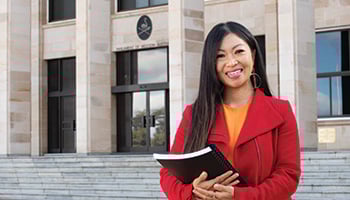 Person standing with documents in arms in front of Parliament House WA