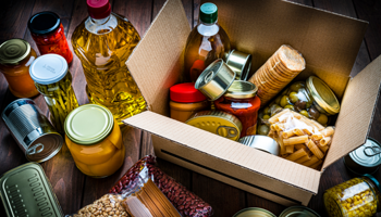 Various foods in bottles cans tins and packaging in and around a box